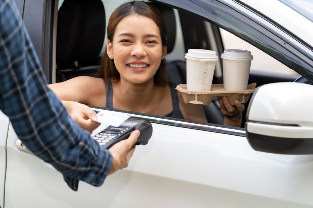 A woman pays by card out of her car window for two coffees 1