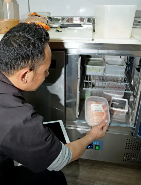 Employee in kitchen adding food into a fridge