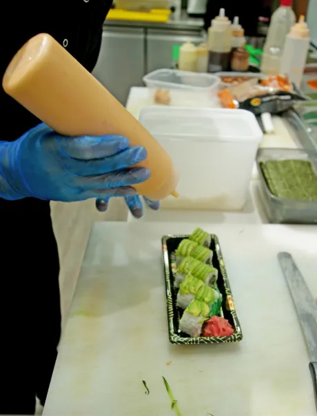 Employee in kitchen adding sauce onto sushi