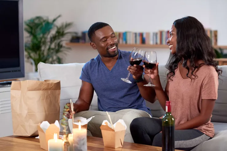 A young couple enjoy takeout food at home with red wine min