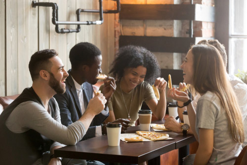 A group of friends eat pizza and drink coffee around a cafe table