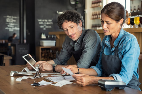 A man and woman go through receipts with a tablet in a restaurant setting