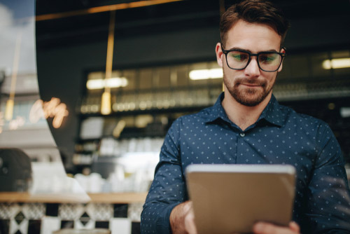 A man wearing glasses and a navy shirt works in restaurant at a tablet