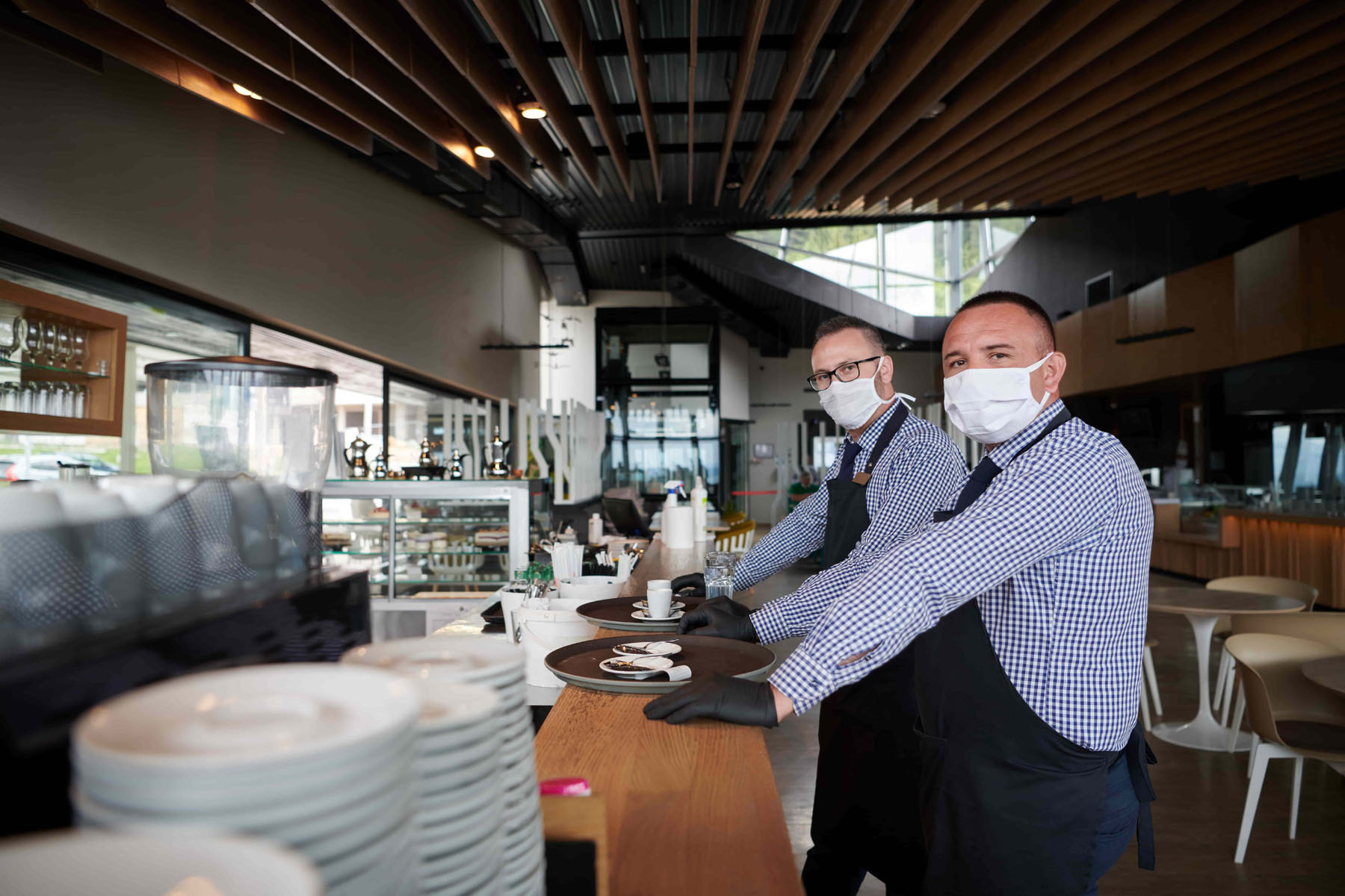 Two masked wait staff at the counter in an empty restaurant min
